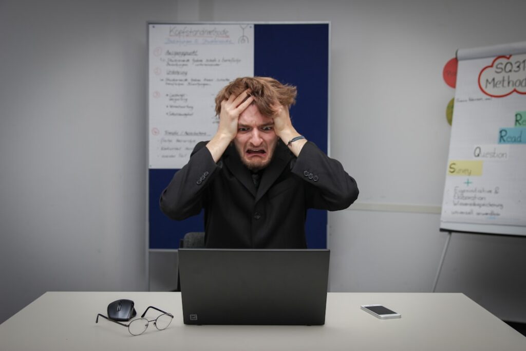 A person sitting at a kitchen table with head in hands, surrounded by paperwork and a coffee mug.