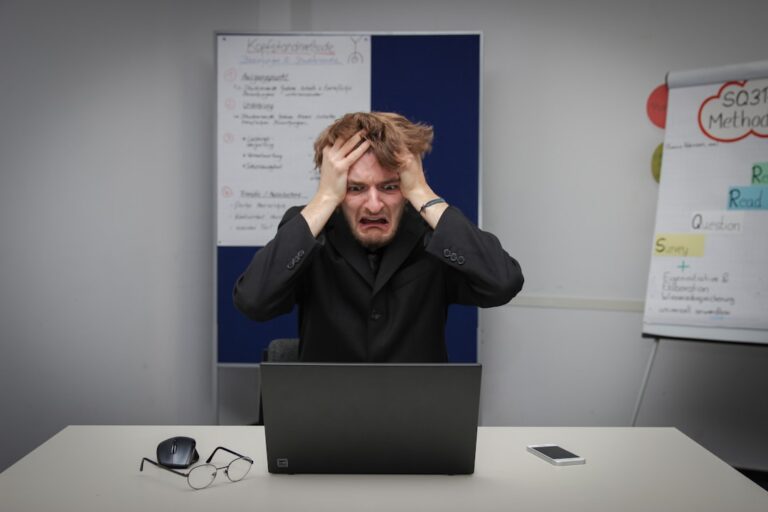 A person sitting at a kitchen table with head in hands, surrounded by paperwork and a coffee mug.