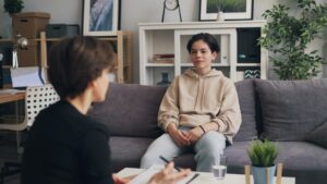 A friend listens quietly while another person talks on a couch in a softly lit living room.