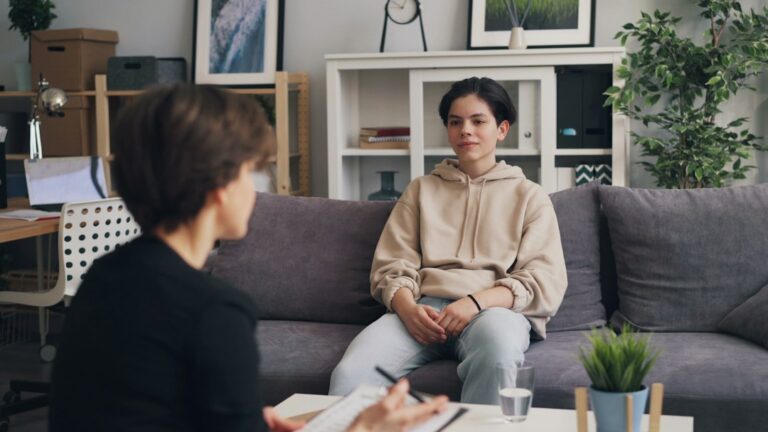 A friend listens quietly while another person talks on a couch in a softly lit living room.