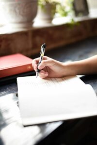 A person sitting indoors by a window writing in a notebook with a peaceful, focused expression.