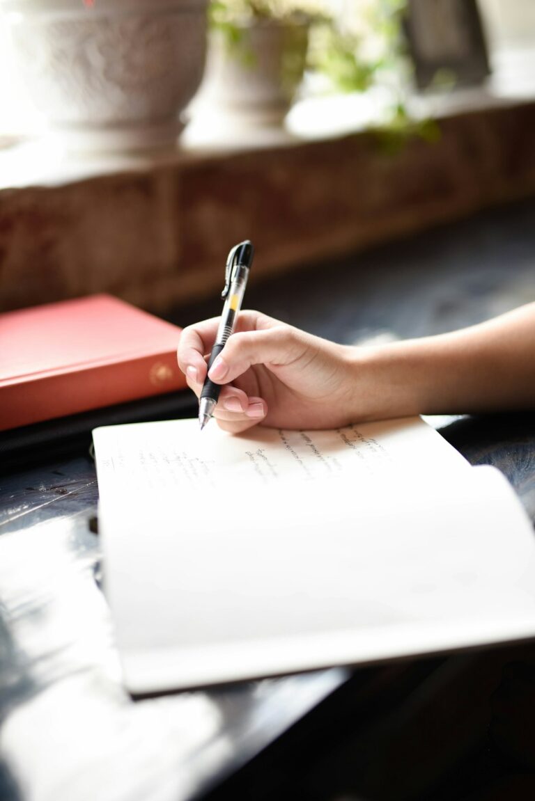 A person sitting indoors by a window writing in a notebook with a peaceful, focused expression.