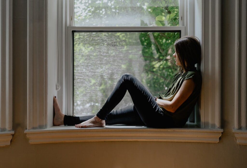A person writing in a journal while a supportive friend sits nearby in a softly lit room.