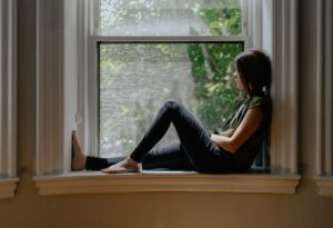 A person writing in a journal while a supportive friend sits nearby in a softly lit room.