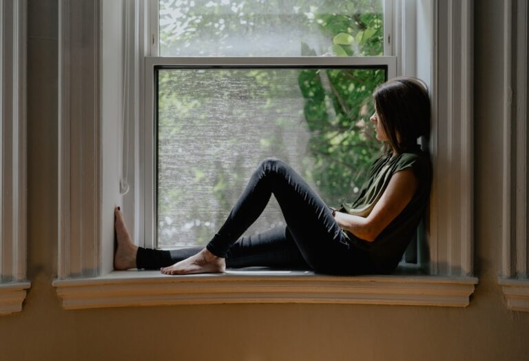 A person writing in a journal while a supportive friend sits nearby in a softly lit room.